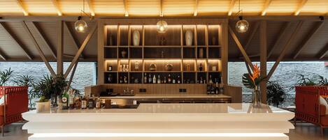 A modern bar area with a wooden ceiling, shelves with bottles, and a view of the sea.