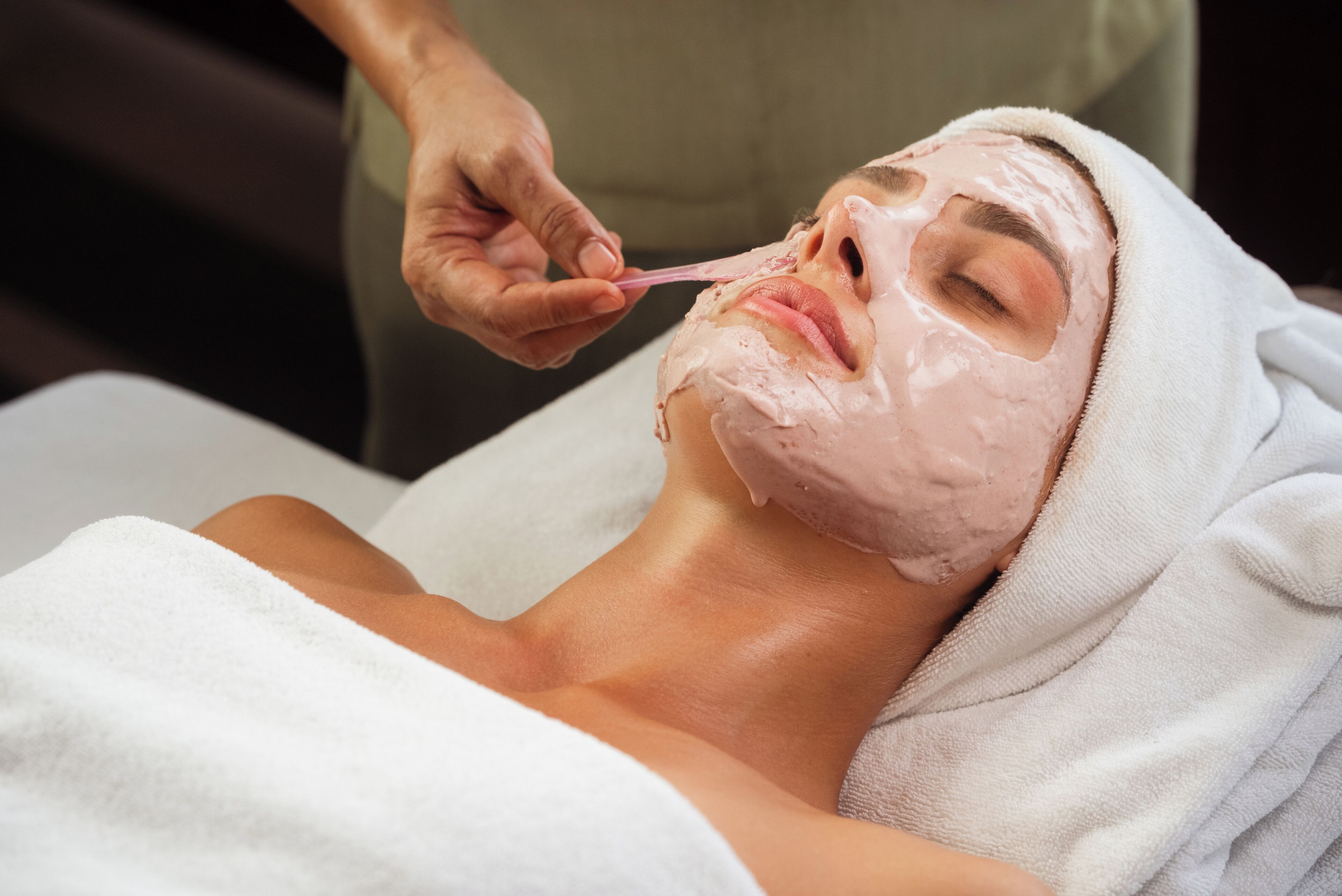 A person lying down with a towel wrapped around their head, receiving a facial treatment.