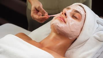 A person lying down with a towel wrapped around their head, receiving a facial treatment.