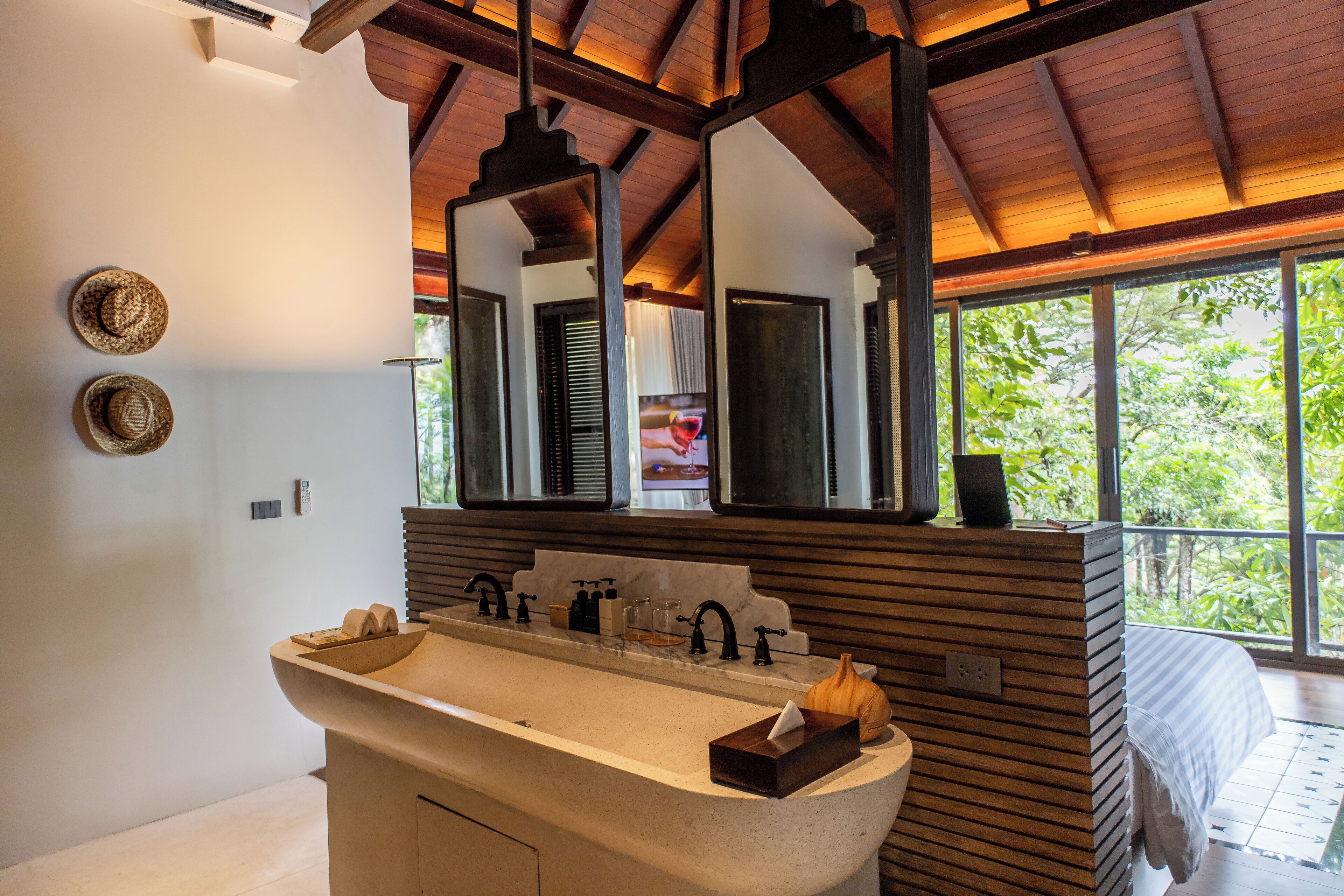 A modern bathroom with a freestanding sink, wooden paneling, a large mirror, and a view of greenery outside.