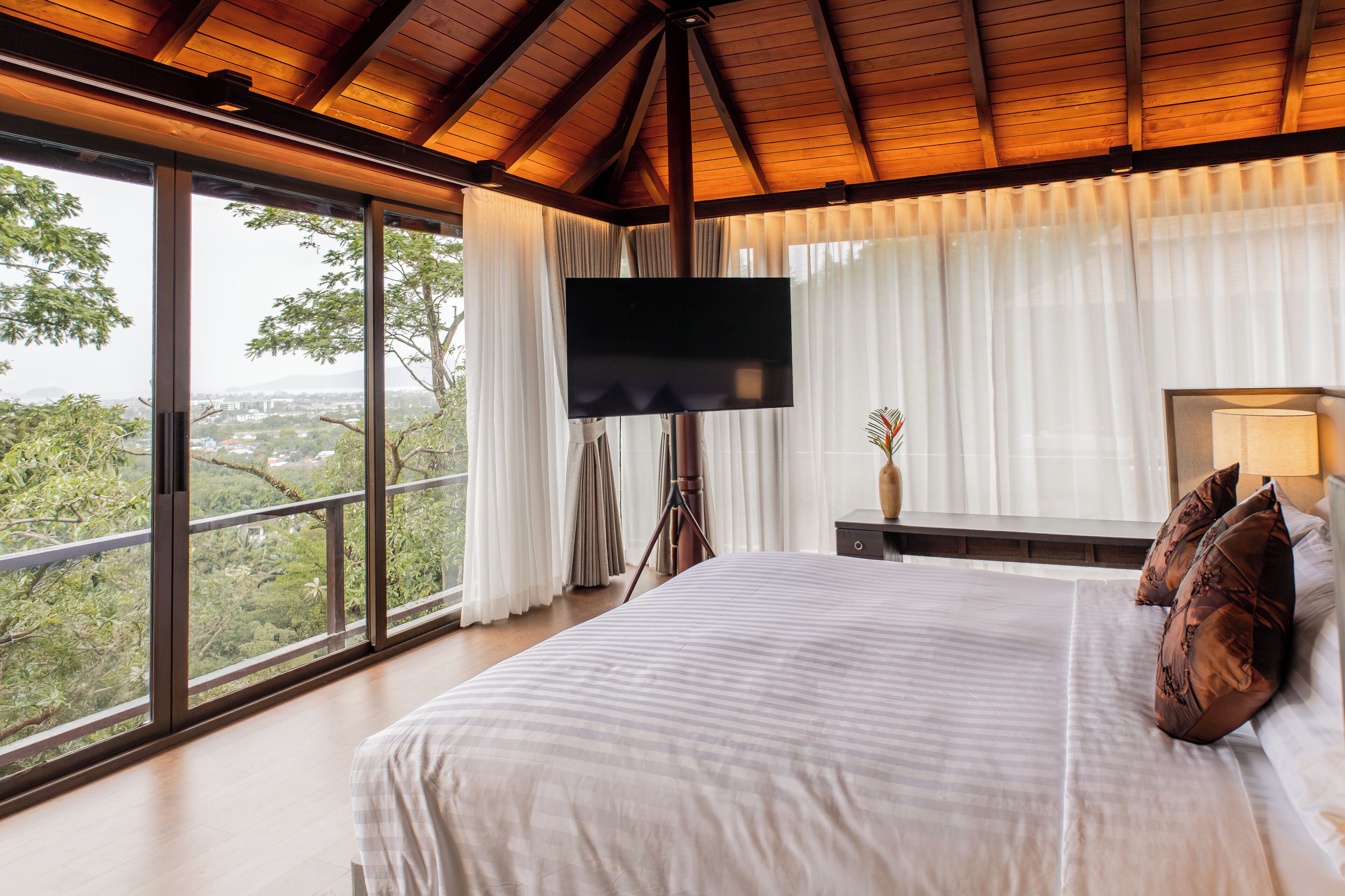 A bedroom with a large bed, a flat-screen TV, and a view of the outdoors.
