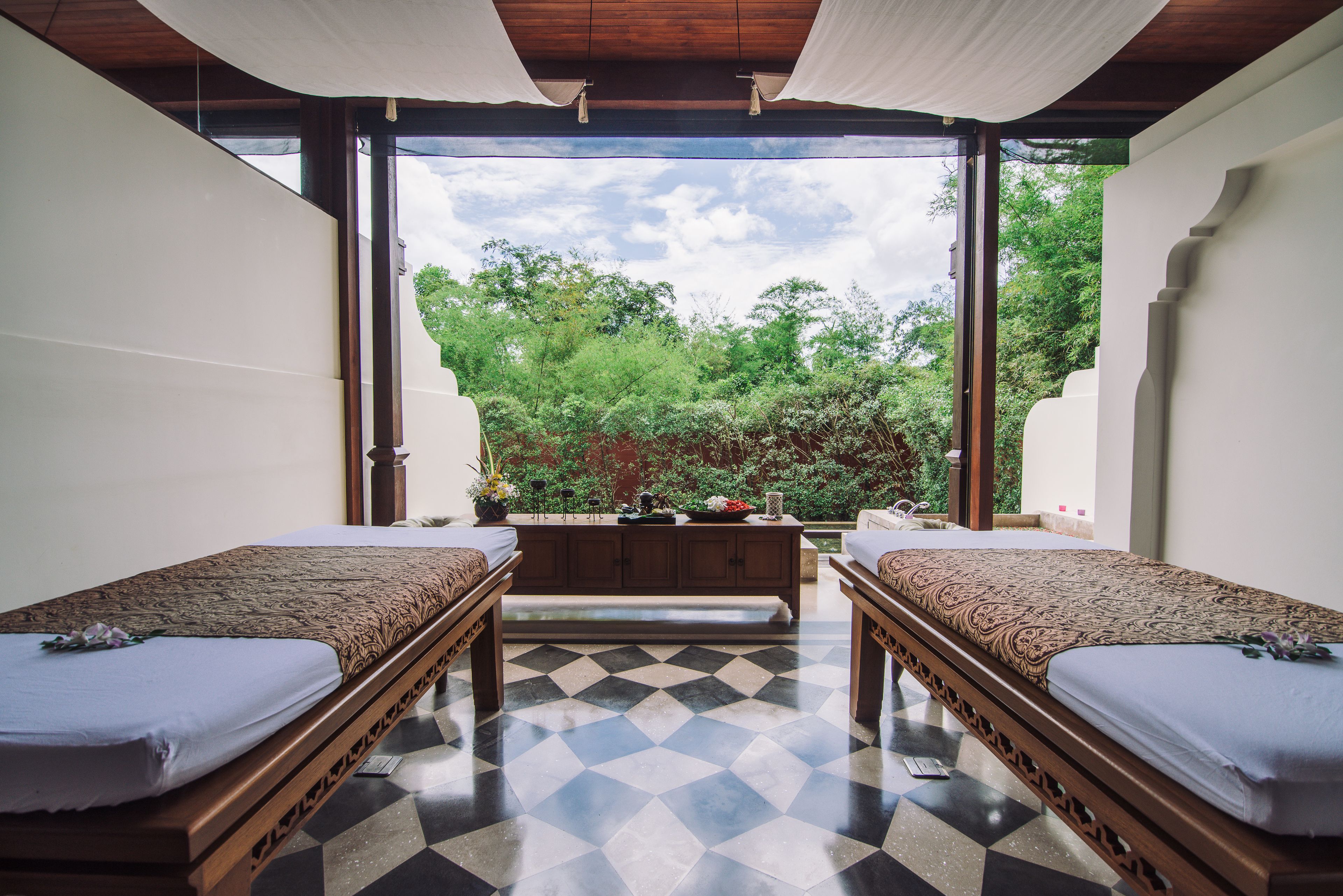 A room with two beds, a bench, and a view of greenery.