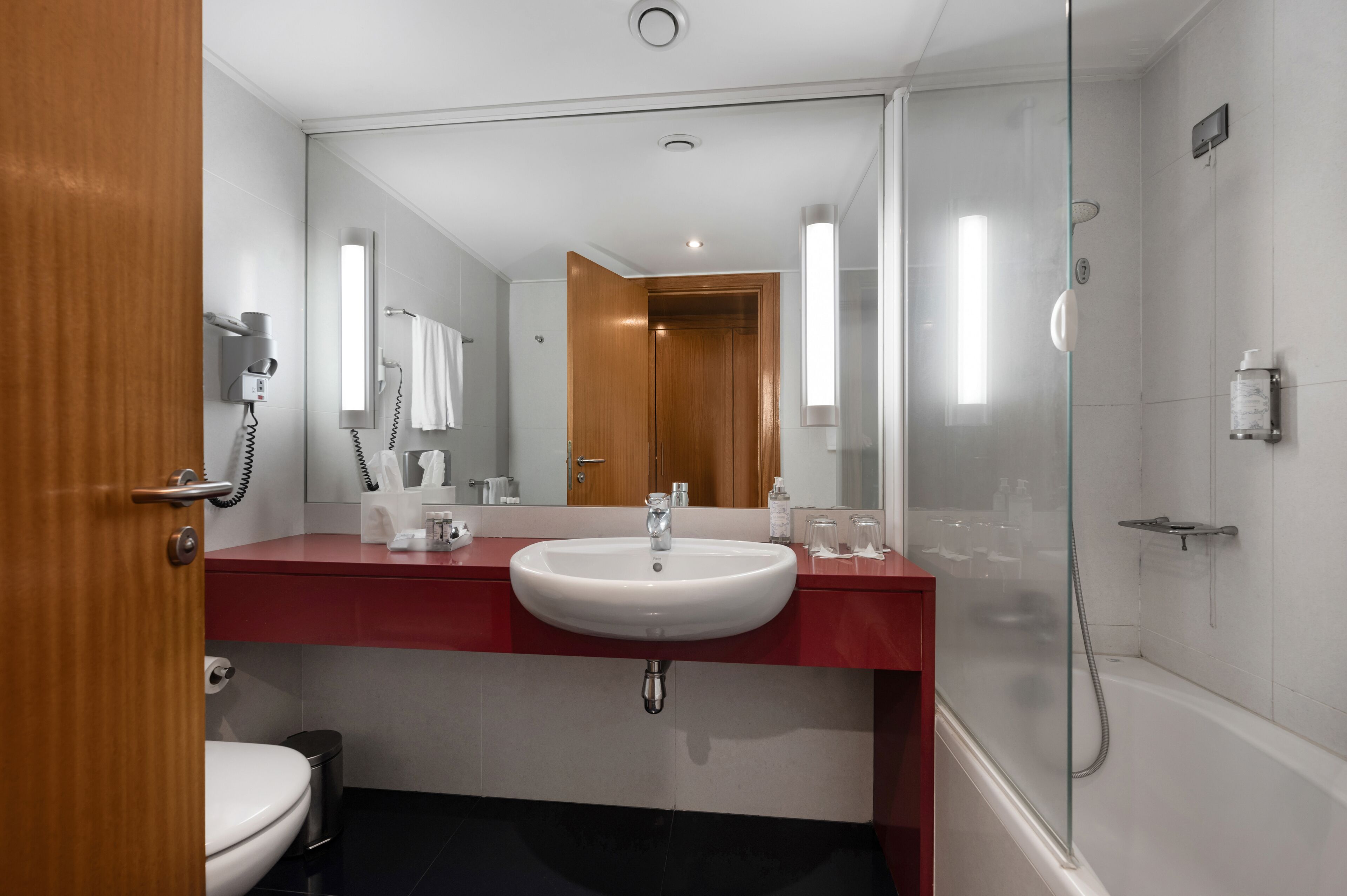 Une salle de bain moderne avec un lavabo blanc, un plan de toilette rouge et une cabine de douche en verre.