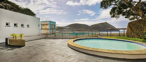 A rooftop pool area with a view of the sea and hills.