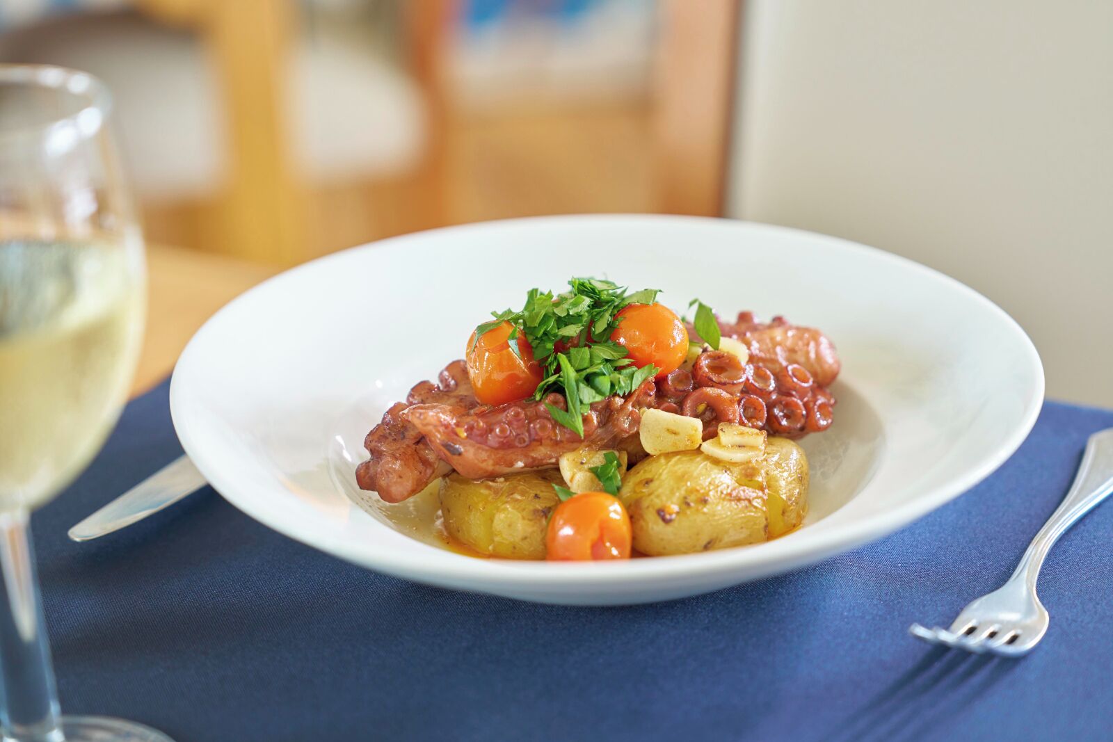 Un plato de comida con carne, patatas y zanahorias, acompañado de una copa de vino blanco.