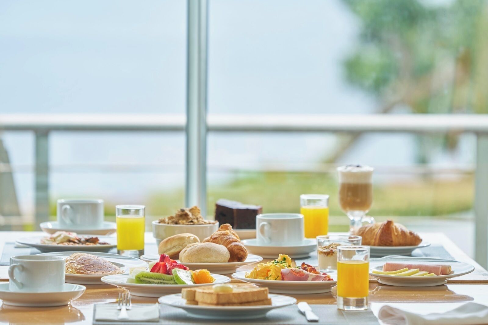 A breakfast buffet with various dishes and beverages on a table with a view of the sea.