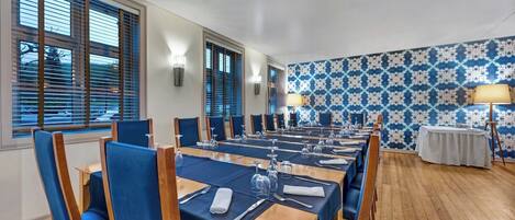 A dining area with long tables, blue upholstered chairs, and a patterned wallpaper wall.
