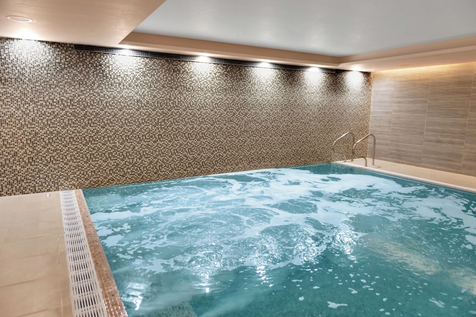 Una piscina interior moderna con un muro de mosaicos y una superficie de agua cristalina.