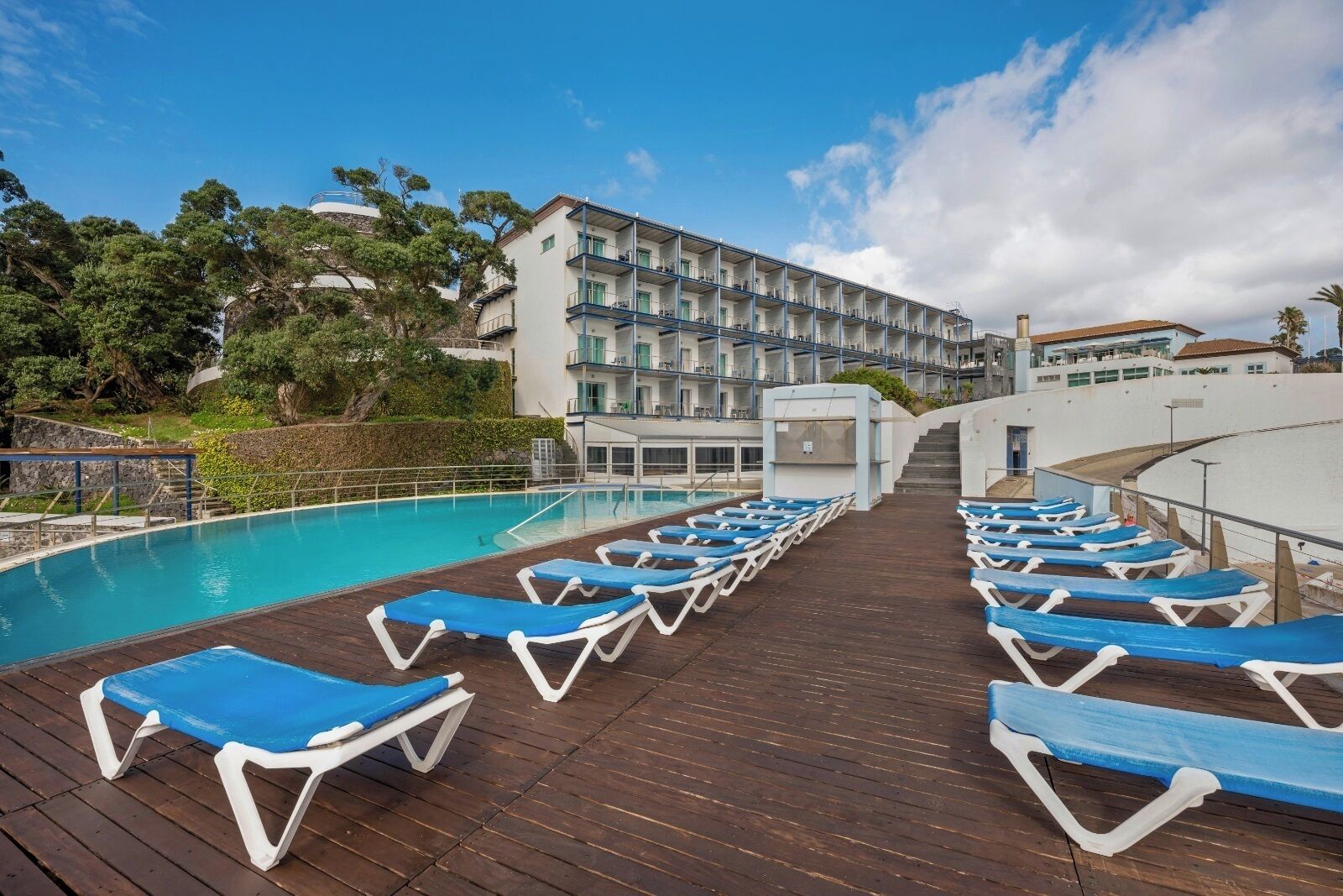 A poolside area with blue lounge chairs, a wooden deck, and a building with multiple balconies.