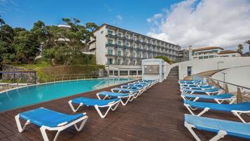A poolside area with blue lounge chairs, a wooden deck, and a building with multiple balconies.