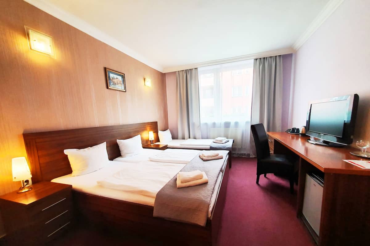 A hotel room with two beds, a desk with a television, and a window with curtains.