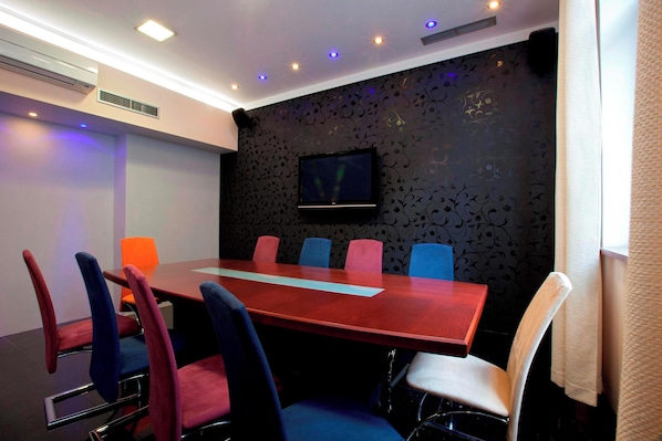 A conference room with a long table, six chairs, a flat-screen TV, and patterned wallpaper.