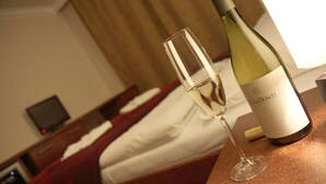 A hotel room with a bed, a bedside table with a wine bottle and glass, and a television on the nightstand.