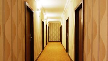 Un pasillo de hotel con papel tapiz estampado, pisos alfombrados y puertas que dan a las habitaciones.