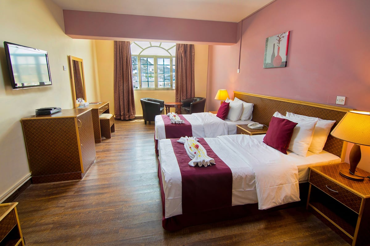 A hotel room with two beds, a desk, a chair, a TV, and a window with curtains.