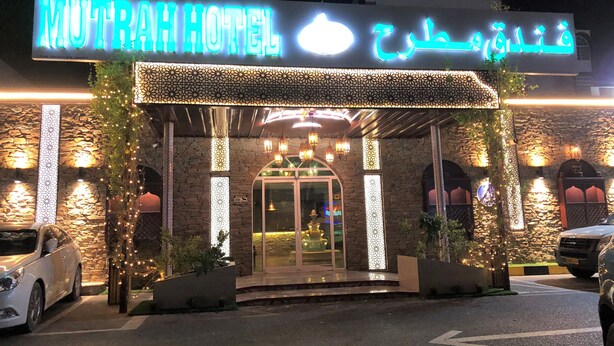 The exterior of MuTrah Hotel with a stone facade, illuminated signage, and a glass entrance.