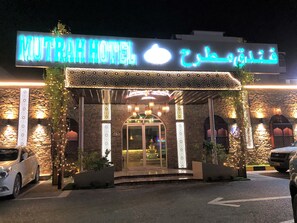 The exterior of MuTrah Hotel with a stone facade, illuminated signage, and a glass entrance.