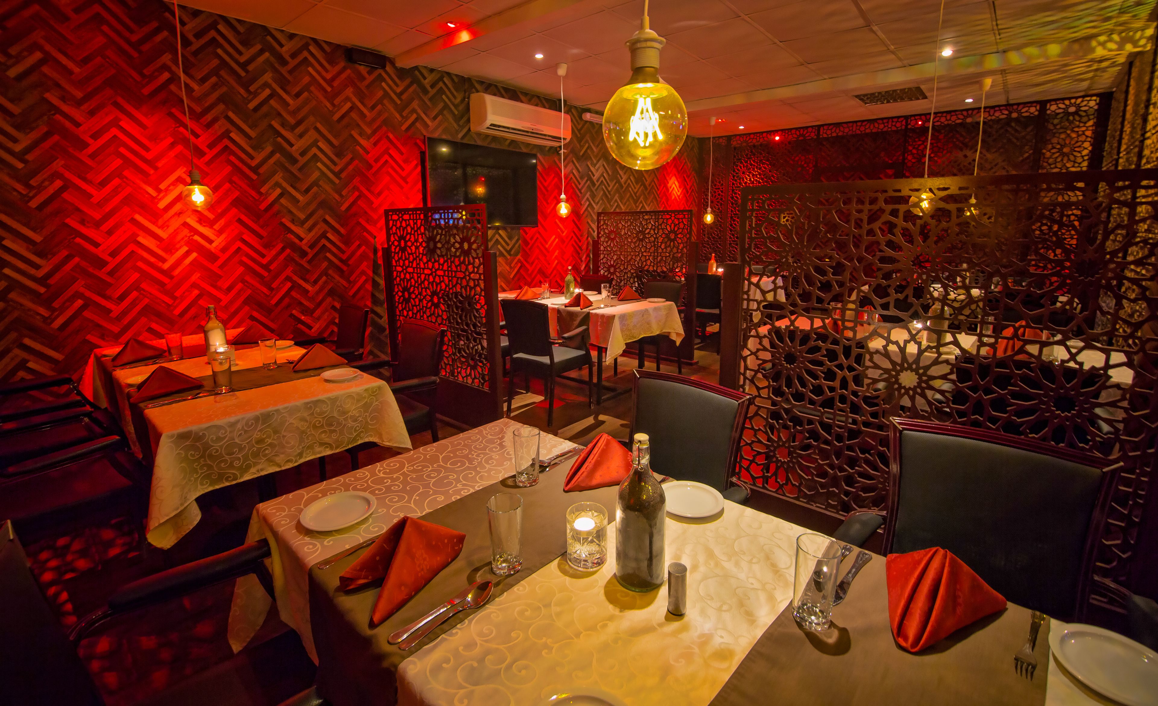 Interior de restaurante con paredes de estampado rojo y negro, luces colgantes y mesas dispuestas para comer.
