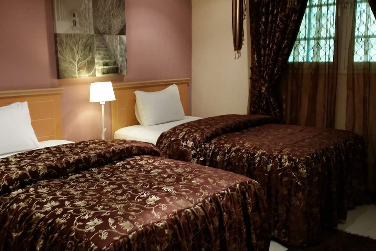 A hotel room with two beds, each with a patterned bedspread, a nightstand with a lamp, and a wall-mounted painting.
