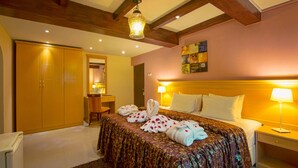 A hotel room with a large bed, wooden ceiling beams, a headboard, and a bedside table with a lamp.