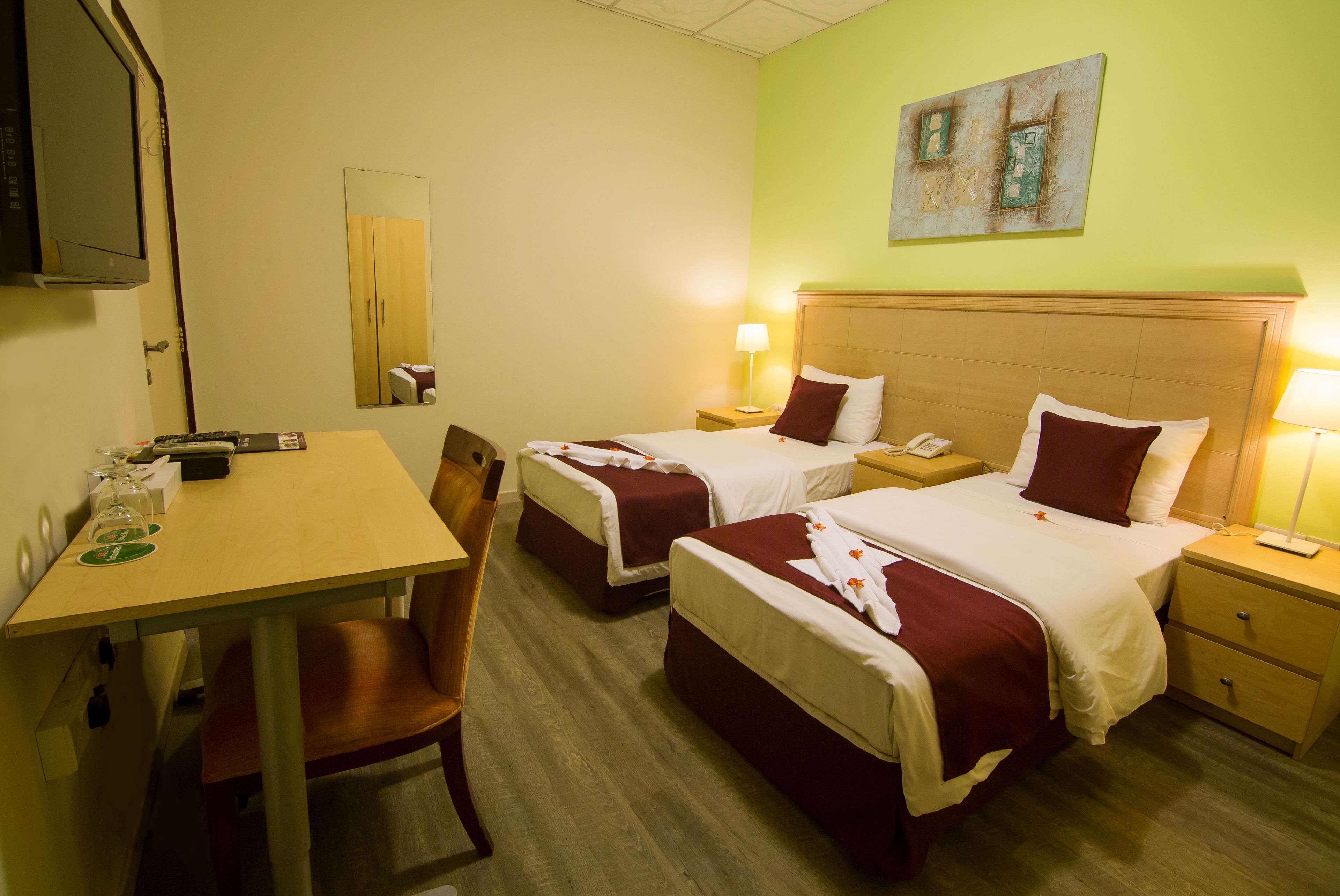 A hotel room with two beds, a desk, a chair, a TV, and a painting on the wall.