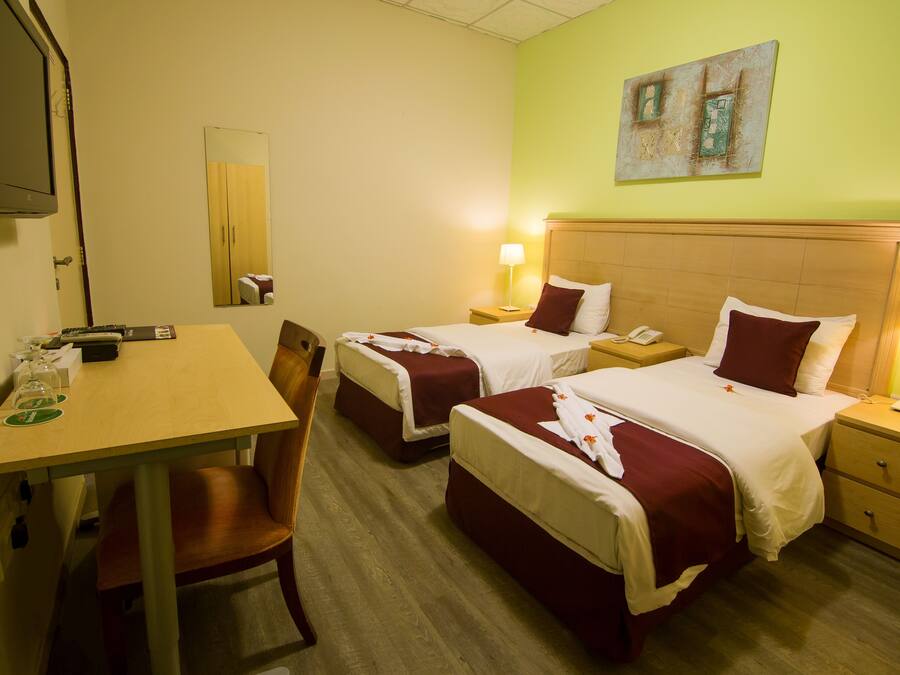 A hotel room with two beds, a desk, a chair, a TV, and a painting on the wall.