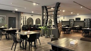A modern restaurant with a mix of seating options including tables and a sofa. There are potted plants and a large decorative structure in the center.