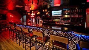 A bar area with a patterned bar counter, multiple hanging light fixtures, and a television screen.