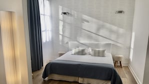 A modern hotel room with a large bed, a bedside table, a floor lamp, and a view of the outside through sheer curtains. - Logis Hôtel Le Plantagenêt (Chinon)