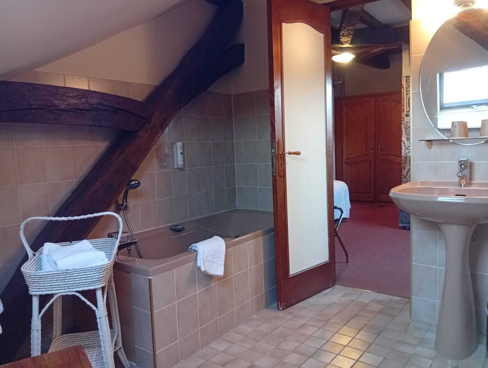 A bathroom with a bathtub, a sink, a mirror, and a wicker chair.