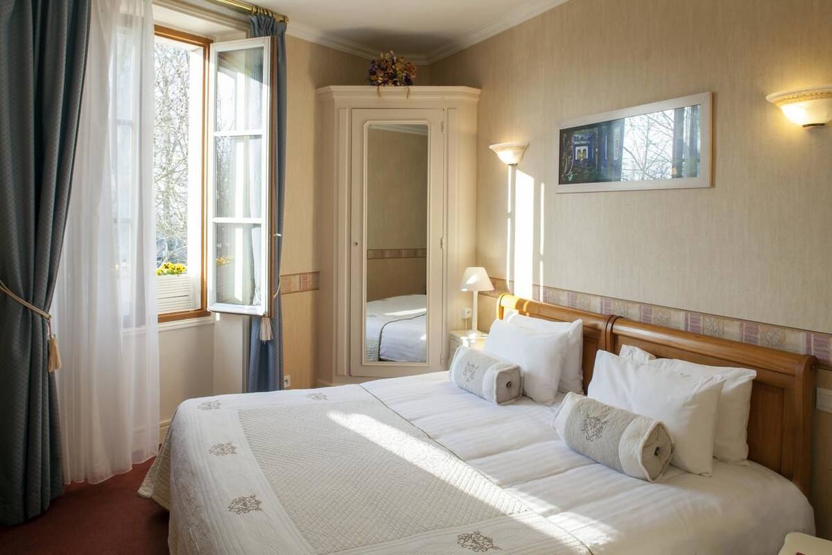 Ein Hotelzimmer mit einem großen Bett, einem Nachttisch mit Lampe, einem Spiegel an der Wand und einem Fenster mit Vorhängen.