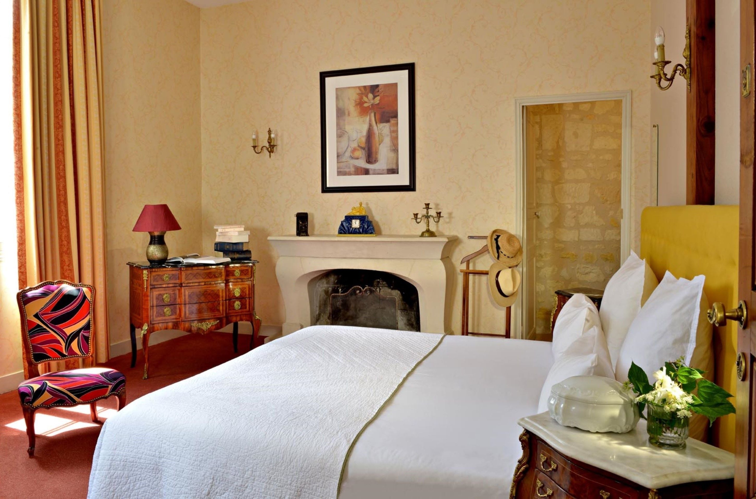 Une chambre d’hôtel avec un lit, une cheminée, un bureau avec une lampe, une chaise et une porte.