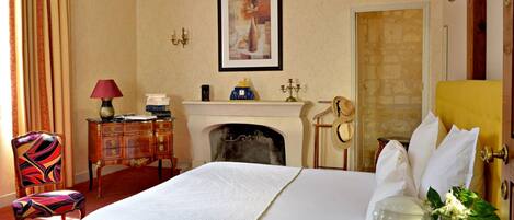 Une chambre d’hôtel avec un lit, une cheminée, un bureau avec une lampe, une chaise et une porte.