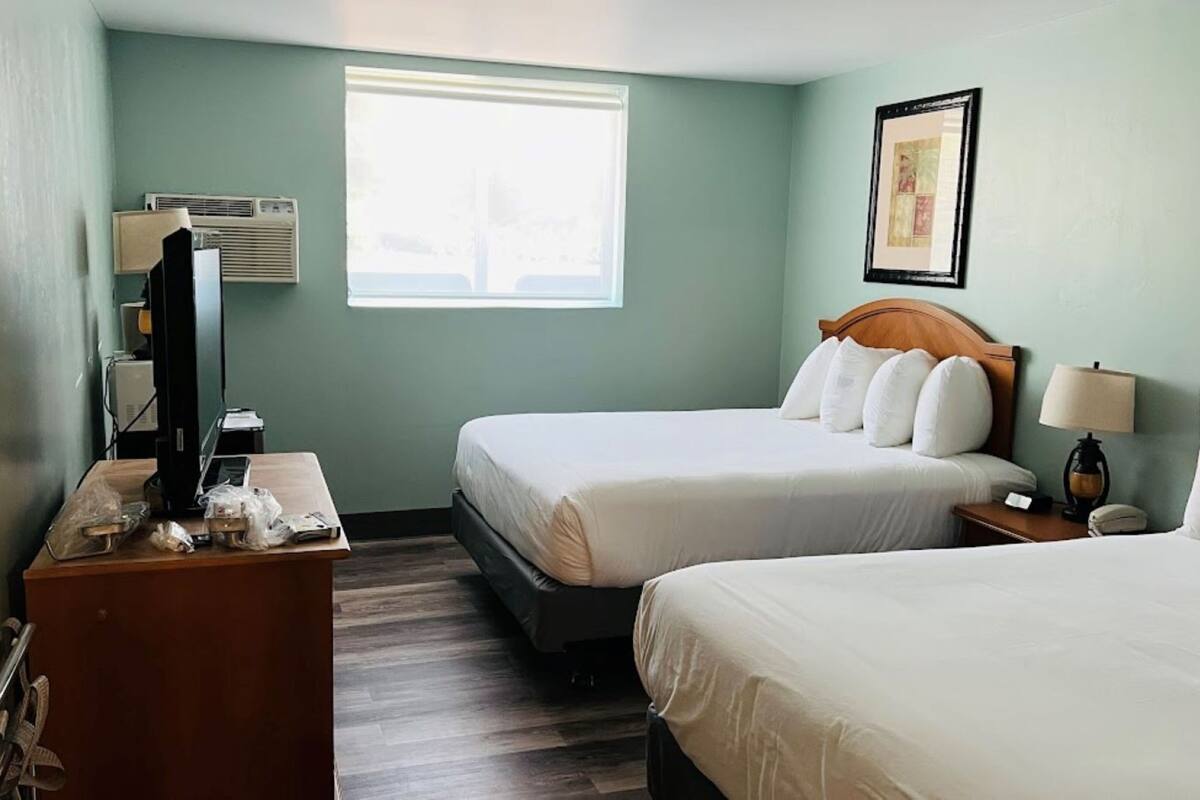 Une chambre d’hôtel avec deux lits, un bureau avec un ordinateur, une fenêtre et un climatiseur fixé au mur.