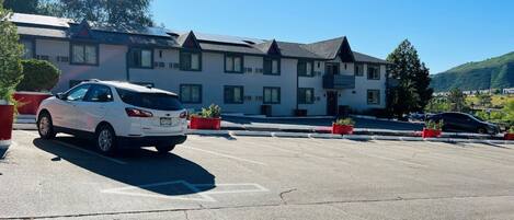 A parking lot with a white car parked in front of a building with multiple windows and a sloped roof.