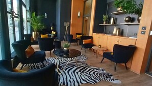 A modern lounge area with leather chairs, a zebra-patterned rug, and a glass wall offering a city view. - Residhome Monceau (Bois-Colombes)