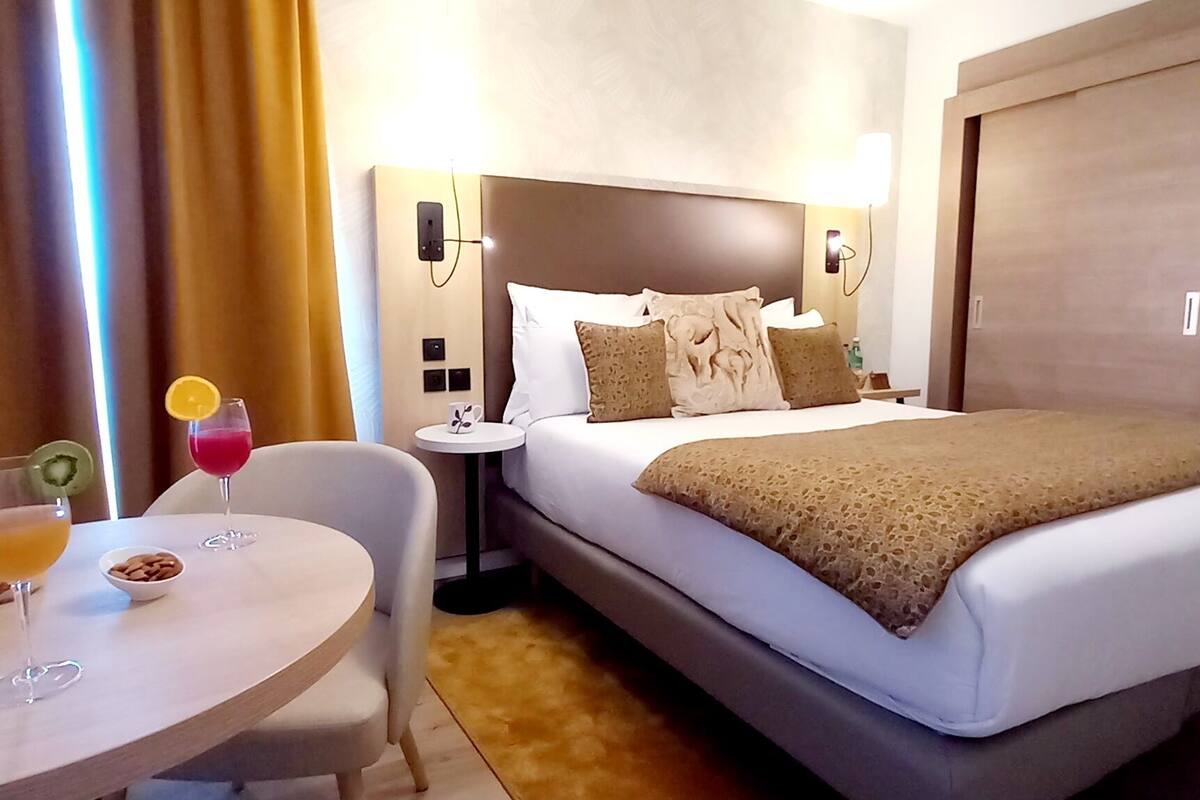 Une chambre d’hôtel avec un lit, une table de chevet et une petite table ronde sur laquelle se trouvent une boisson et des en-cas.