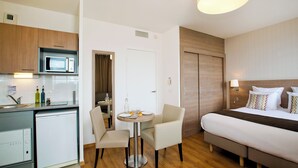 A hotel room with a bed, bedside table, lamp, and a kitchenette with a microwave and dishwasher. - Residhome Monceau (Bois-Colombes)