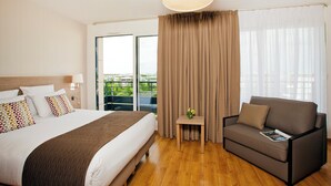 A hotel room with a bed, a sofa, a small table with a vase, and a large window with curtains. - Residhome Monceau (Bois-Colombes)