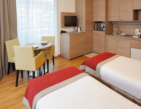 A hotel room with two beds, a dining table with chairs, a kitchenette, and a TV. - Residhome Monceau (Bois-Colombes)