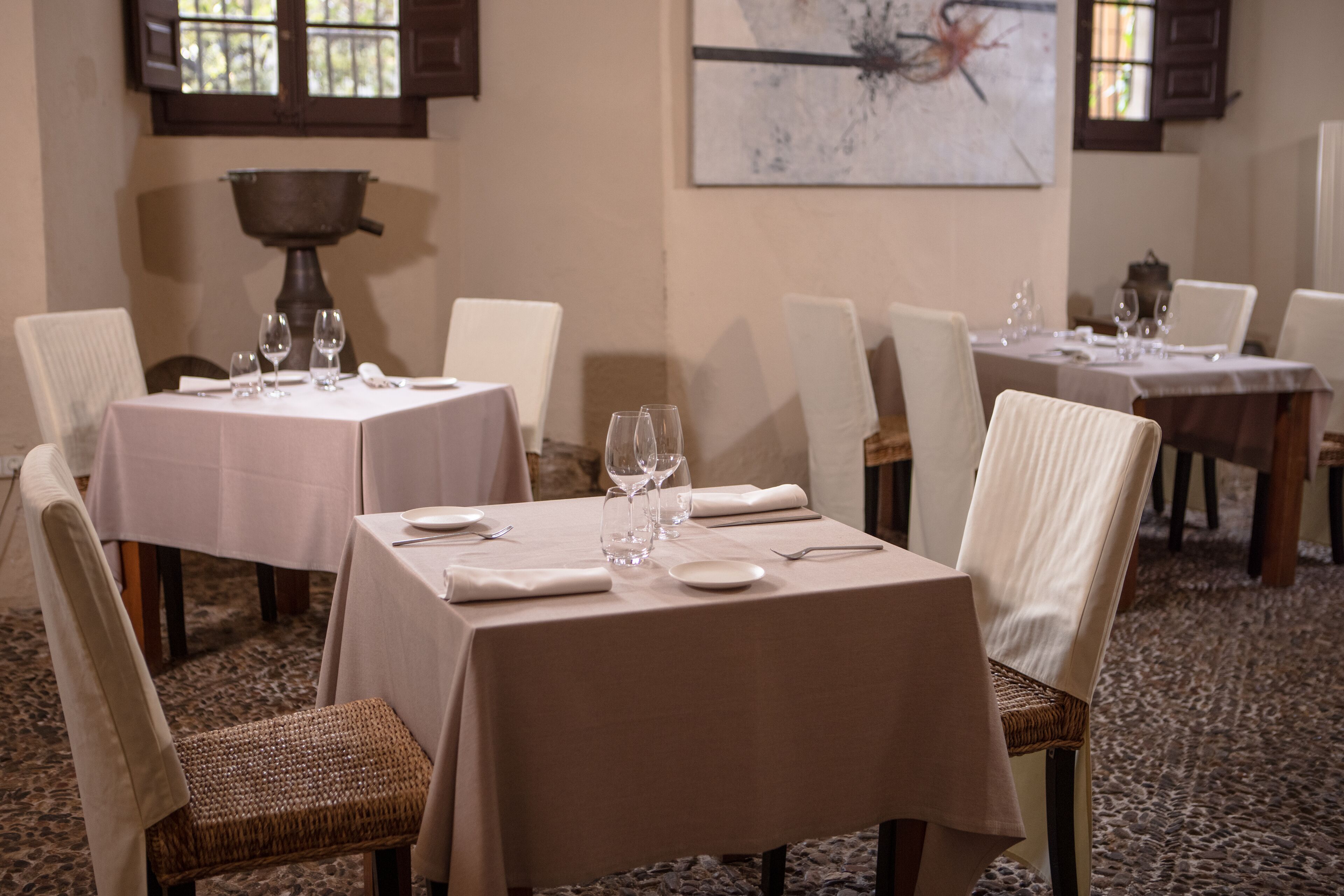 Uma sala de jantar com mesas preparadas para dois, cada uma com toalha branca, cadeiras brancas e copos de vinho.