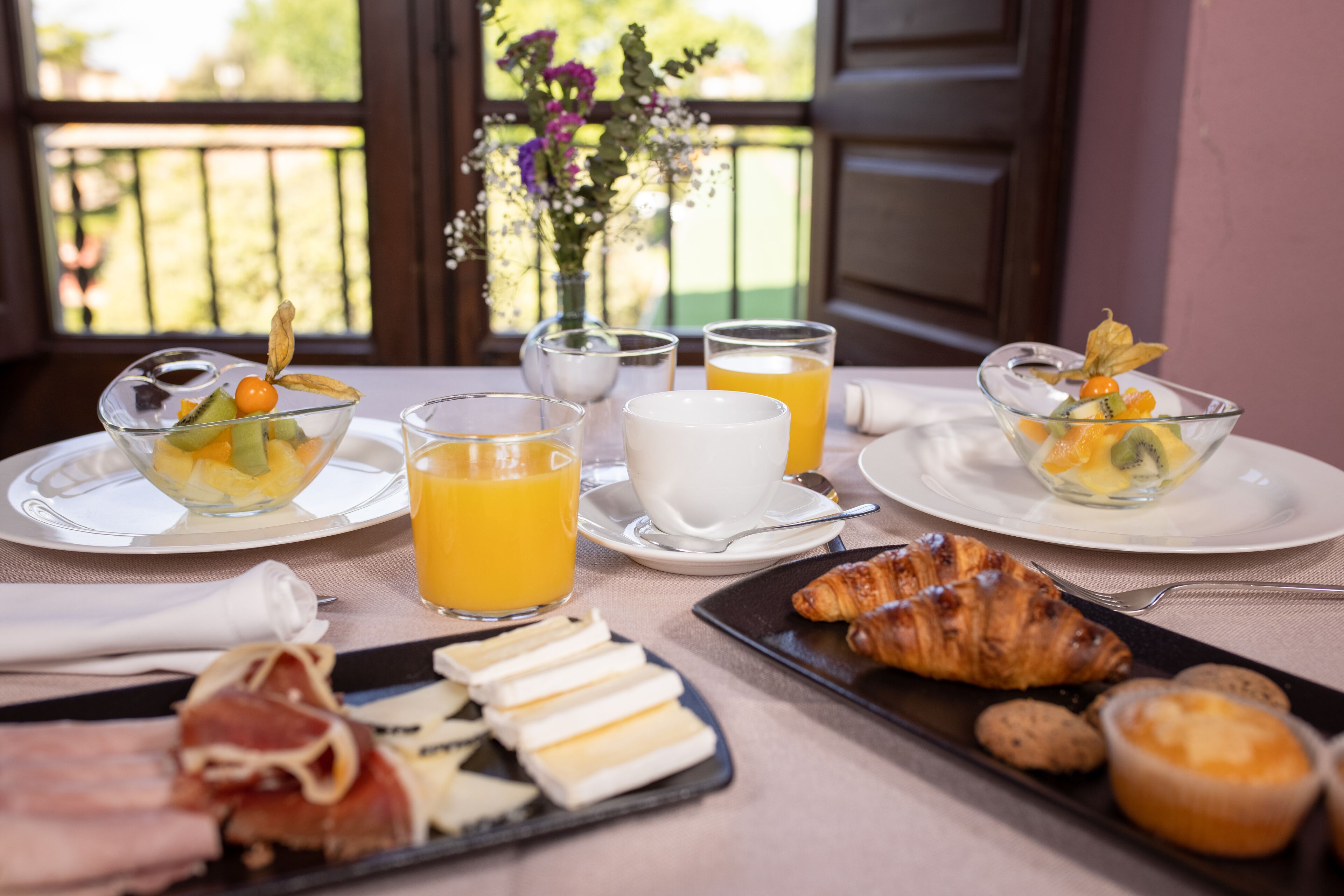 Un plateau de petit-déjeuner avec un croissant, des fruits et du fromage, ainsi que des verres de jus d’orange et une tasse de lait.