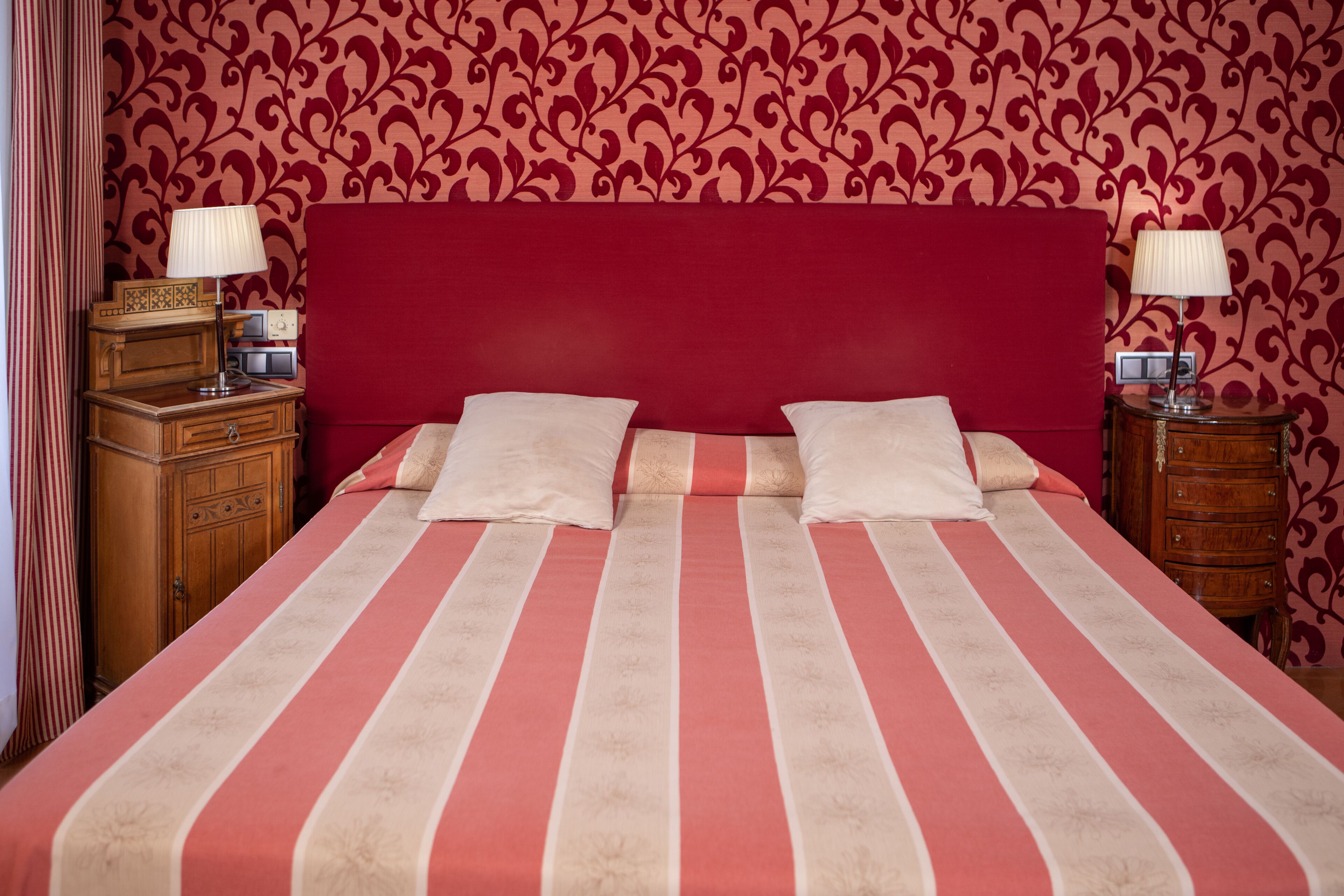 Una habitación de hotel con una cama grande, dos mesitas de noche y un cabecero rojo.