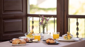 A breakfast table with various dishes, drinks, and a vase of flowers.