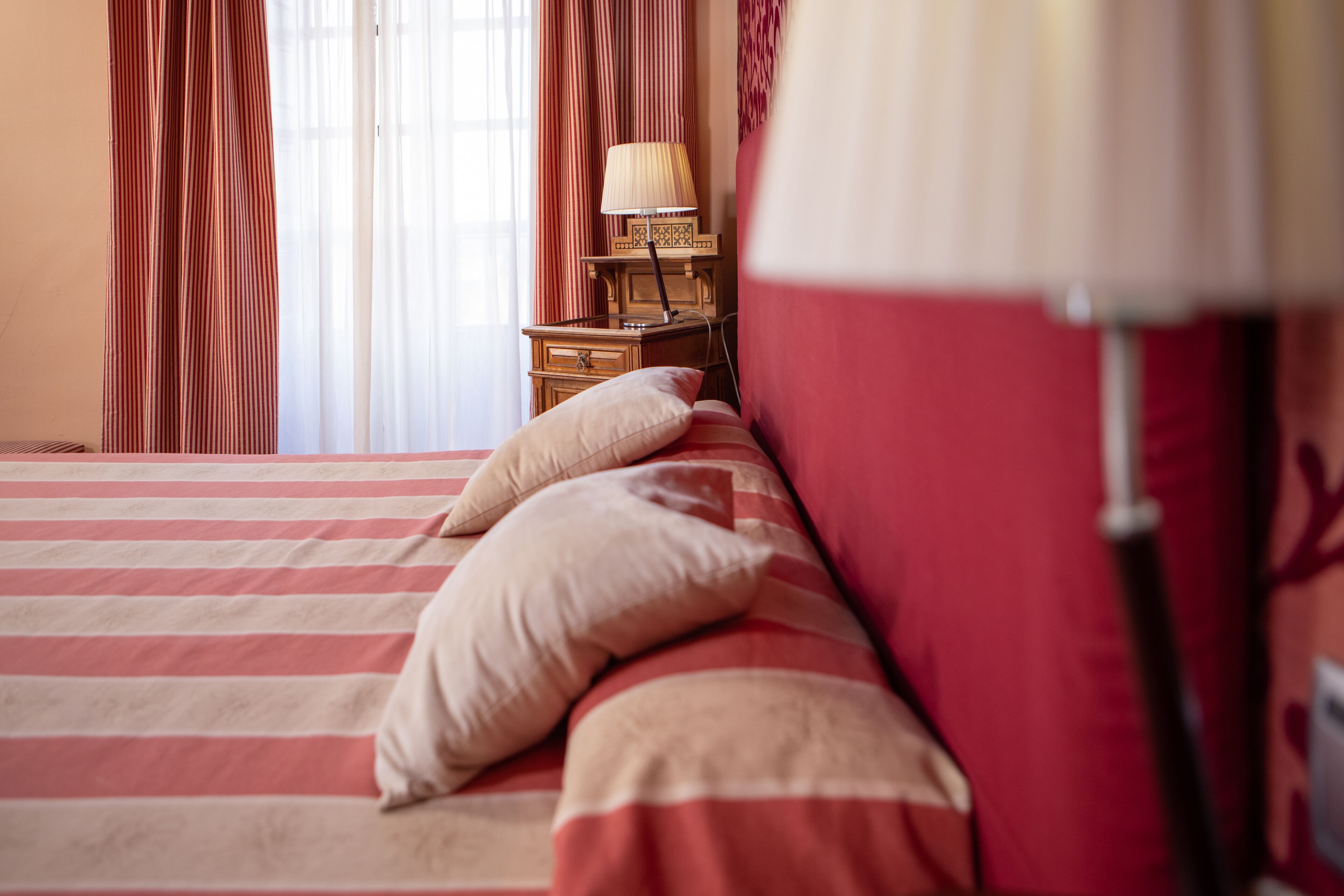 Una cama con ropa de cama a rayas y almohadas, una mesita de noche con lámpara y cortinas.