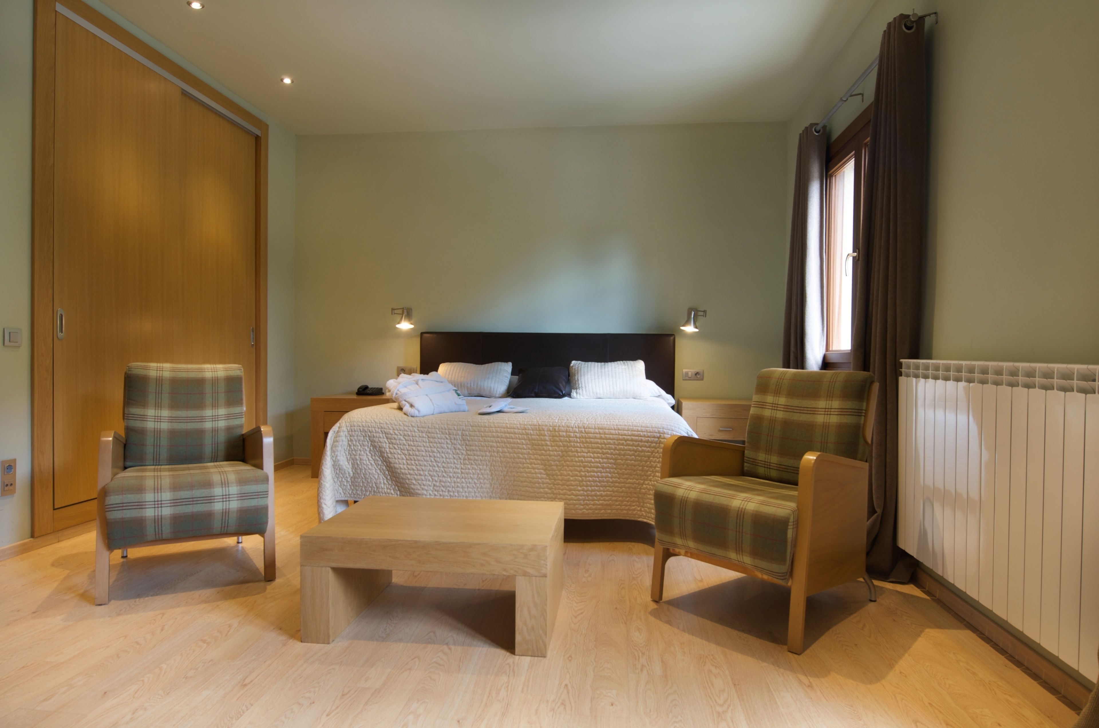 A bedroom with a bed, two armchairs, a wooden bench, a wardrobe, and a radiator.