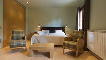 A bedroom with a bed, two armchairs, a wooden bench, a wardrobe, and a radiator.