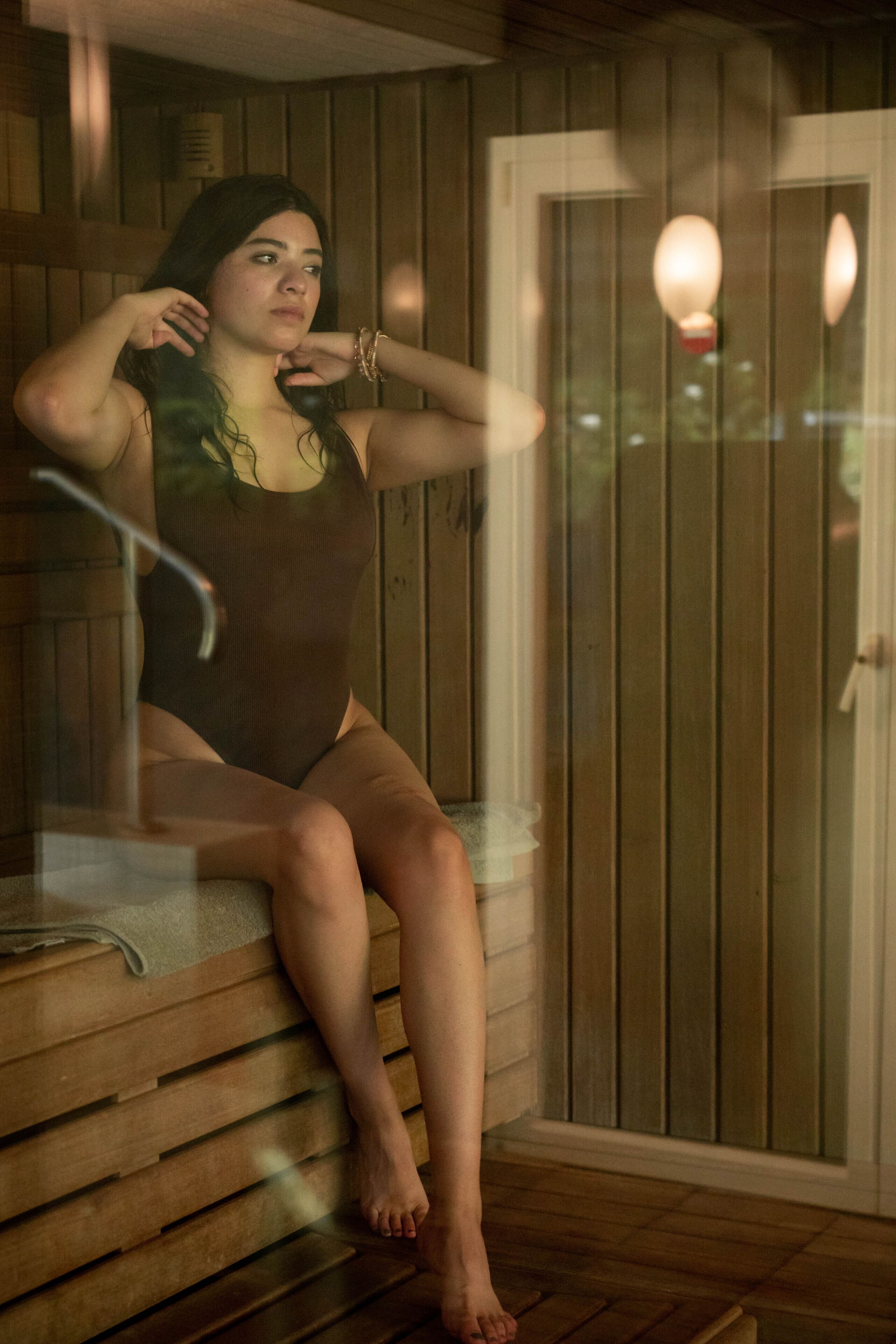 A person sitting on a bench in a room with wooden walls and a door.