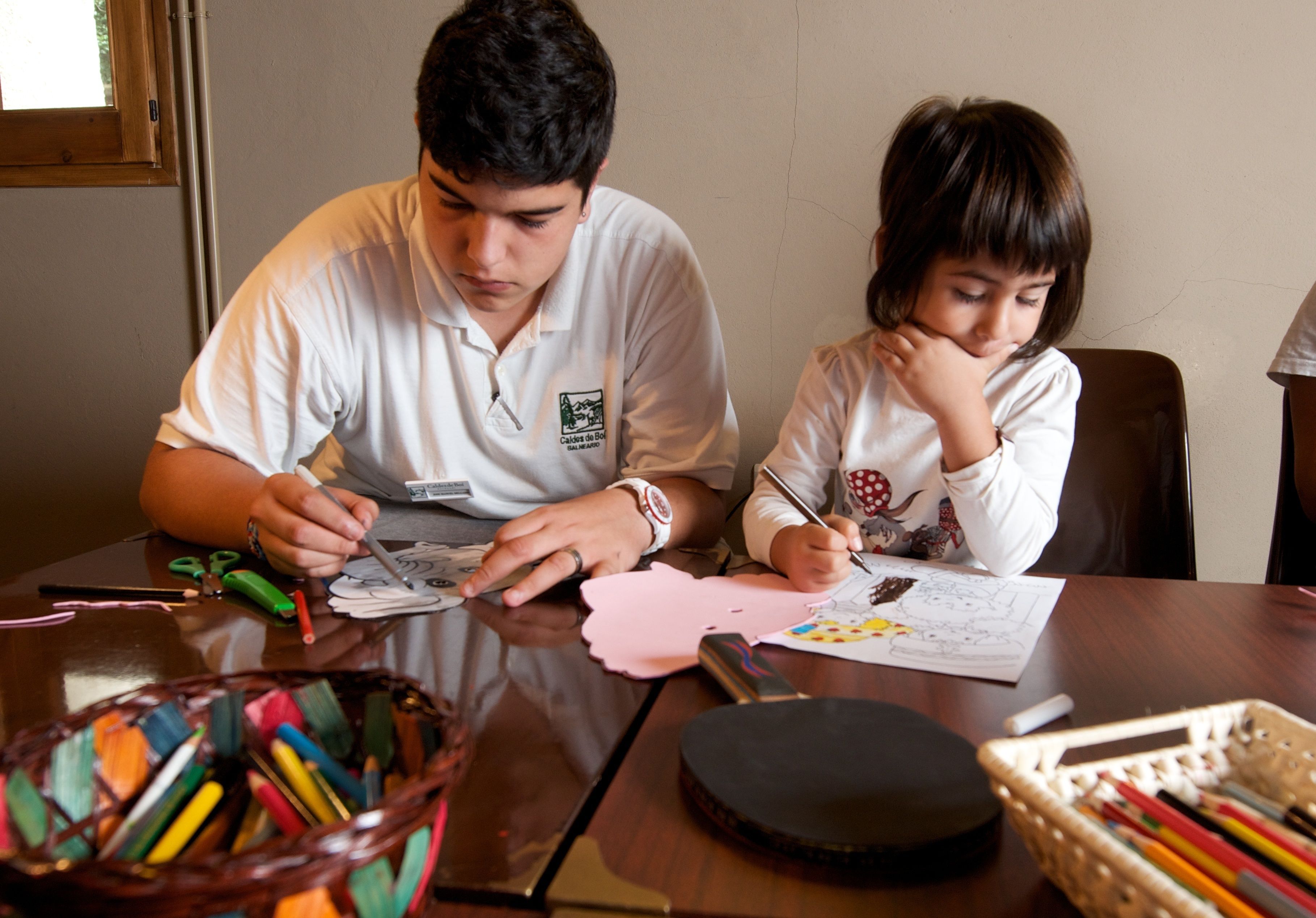 Two people sitting at a table with drawing materials and colored pencils.