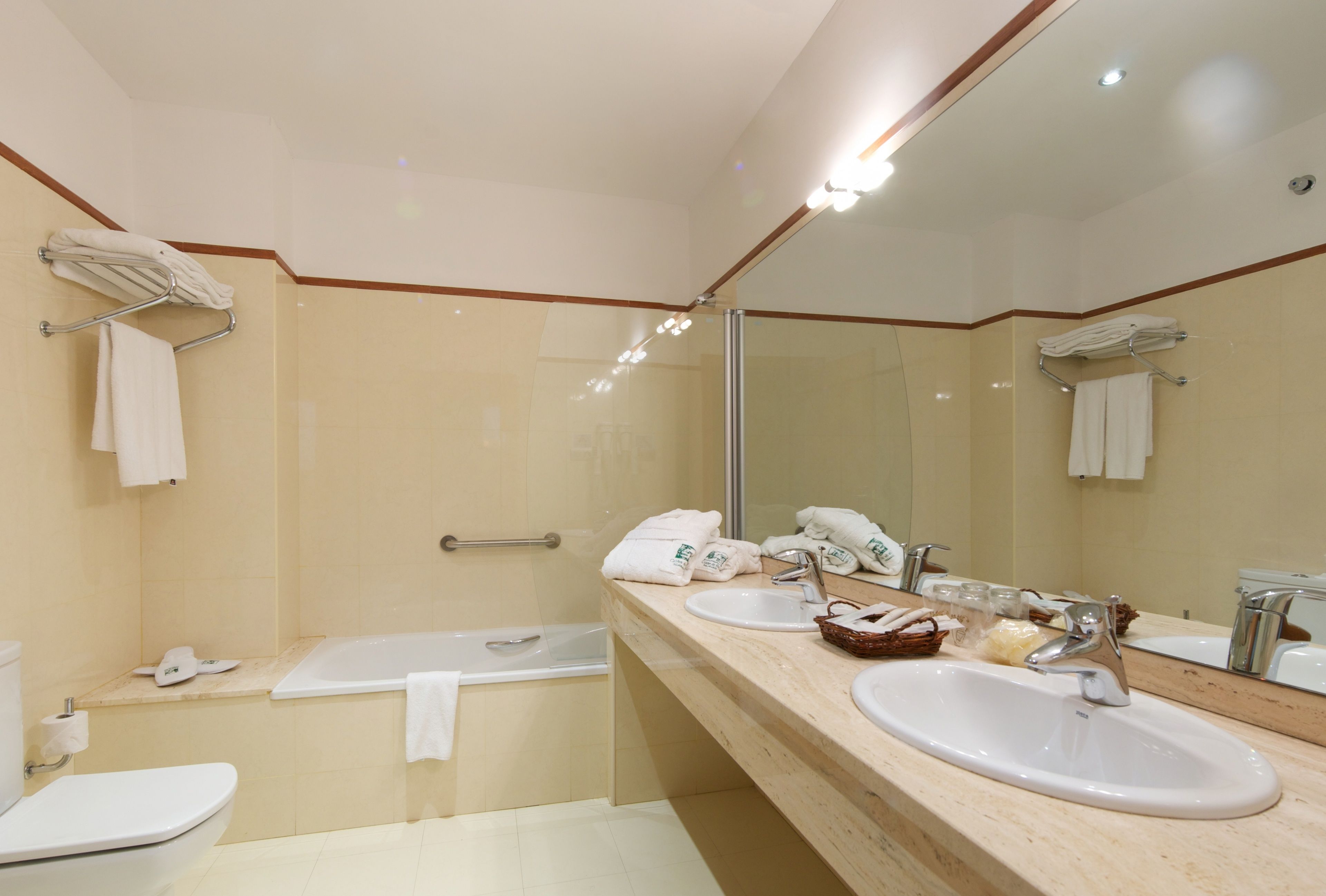 A modern bathroom with a bathtub, two sinks, a large mirror, and towel racks.